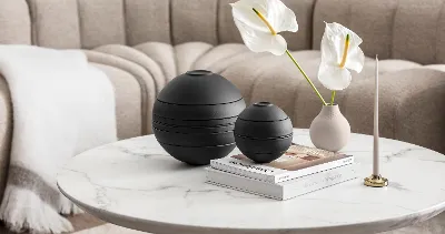 A beige coffee table with the black La Boule in 2 sizes in front of a beige sofa with a white blanket.