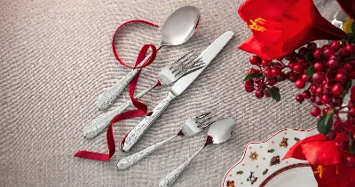 Komplet sztućców Toy's Delight składający się z łyżki, widelca, noża i dwóch małych łyżeczek, ułożony na beżowej tkaninie z czerwoną kokardą.
