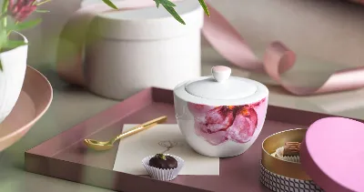 A Rose Garden sugar bowl with a candle, a golden spoon, a chocolate truffle and decorative items on a tray.