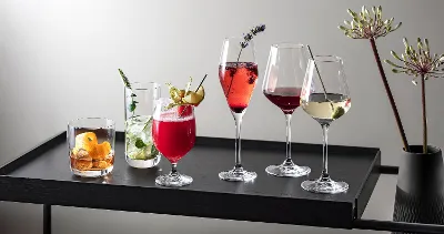 Various drinks in La Divina glasses presented on a modern black tray, decorated with herbs and fruit.