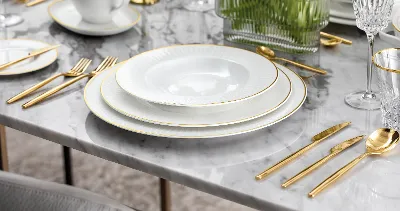 Elegant table decoration with white Château Septfontaines plates, gold MetroChic d'Or cutlery and crystal glasses on a marble table.