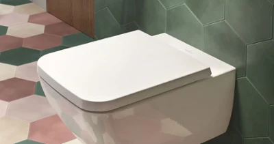 Venticello toilet with a toilet roll holder A modern bathroom with a Venticello toilet, hexagonal green tiles, colourful floor tiles, a wooden shelf and a toilet roll holder on the wall.