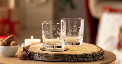 Dwie szklanki Toy's Delight na drewnianym krążku Dwie szklanki Toy's Delight na drewnianym krążku, świeca i miska orzechów włoskich na stole.