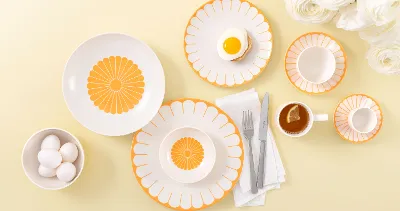 Table setting with Villeroy & Boch Fleur Soleil plates, eggs, tea with a slice of lemon, and white flowers on a light yellow background.