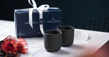 Deux coupelles de collier noires et un morceau de fleur Deux tasses à collier noires sur une table avec un paquet cadeau, à côté d'une fleur rouge et noire.