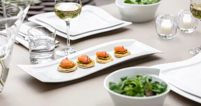 A table set for a meal with plates of appetizers, glasses of white wine, a bowl of salad, and tea lights.