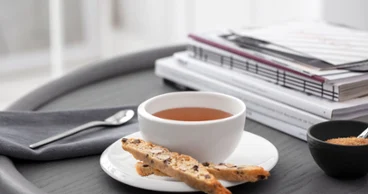 A NewMoon teacup and saucer with biscotti on a tray next to books and a spoon.