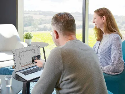 Miejsce pracy z dwiema osobami Dwie osoby siedzą przed laptopem. Mężczyzna wskazuje na ekran.