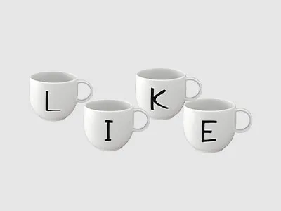 Vier weiße Tassen mit jeweils einem Buchstaben darauf, die so angeordnet sind, dass sie vor einem grauen Hintergrund das Wort „LIKE“ ergeben.