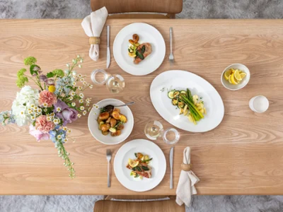 Vista superior de una mesa inspirada en la primavera con la colección For Me de Villeroy & Boch. Incluye cuencos franceses, platos llanos, un cuenco redondo para servir y una fuente ovalada – todo lleno de comida fresca y de temporada. Los cubiertos Piemont acompañan elegantemente cada lugar. La mesa de madera natural y un centro de flores suaves crean un ambiente relajado y contemporáneo.