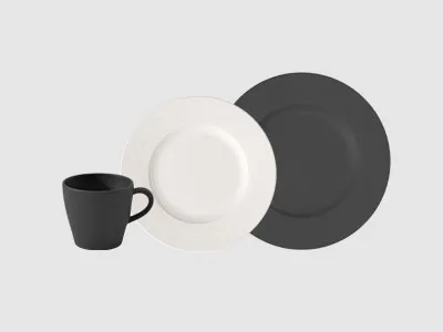 Eine schwarze Tasse, ein weißer Teller und ein schwarzer Teller sind zusammen auf einem schlichten hellgrauen Hintergrund angeordnet.