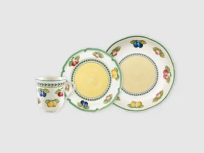 Drei Teile Keramikgeschirr – eine Tasse, ein Salatteller und ein Essteller – mit Obst und grünem Rand verziert.