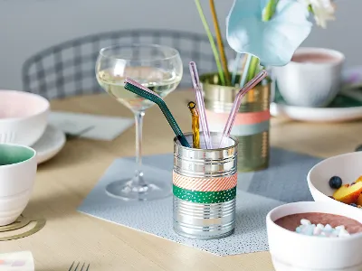 Elegant gedeckter Esstisch mit einem Glas Weißwein, bunten Strohhalmen in einem dekorativen Halter und Schalen mit frischem Obst und Smoothie.