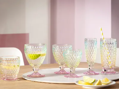 A set of six Villeroy & Boch Boston Pearl glass tumblers on a wooden table with lime and lemon slices, one tumbler with a straw and a lemon slice.