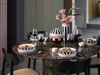 Une table ronde en marbre avec quatre couverts, de la vaisselle Memphis rayée, des verres à vin et un vase avec des fleurs roses