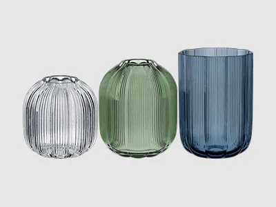 Drei gerippte Glasvasen in unterschiedlichen Höhen und Farben: klar, hellgrün und dunkelblau, nebeneinander angeordnet.