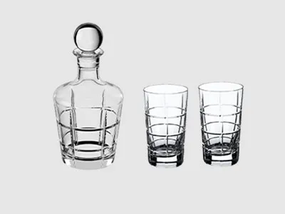 Eine Karaffe aus klarem Glas mit rundem Stopfen neben zwei passenden Bechern aus klarem Glas, alles auf einem schlichten Hintergrund.