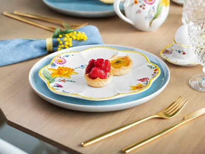 Une table élégamment dressée avec une assiette à dessert Spring Awakening sur laquelle est posée une tartelette aux fruits, une assiette Crafted bleu clair, des couverts de table MetroChic dorés et des verres en cristallin Boston.