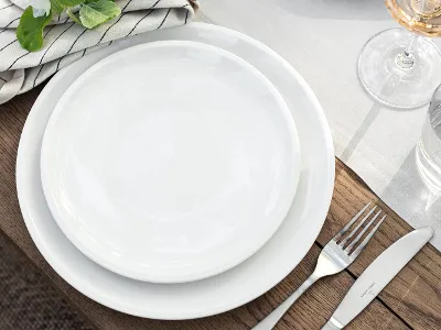 An Artesano wooden table set from Villeroy & Boch with white plates, a fork, a knife, a glass of water, a wine glass, and a striped napkin with green leaves.