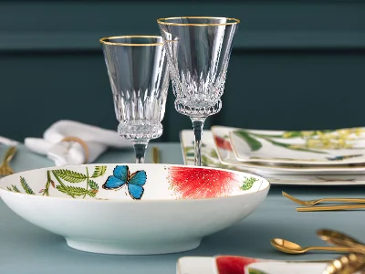 Élégant service de table composé de verres en cristal, d'un bol avec des motifs de papillons et de fleurs et d'assiettes avec des motifs floraux sur fond bleu-vert.