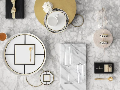 Une vue aérienne d’une table élégamment dressée sur une surface en marbre, avec de la vaisselle MetroChic aux motifs géométriques, une boîte cadeau avec un ruban, des couverts de table dorés, des flûtes à champagne et des articles de décoration.