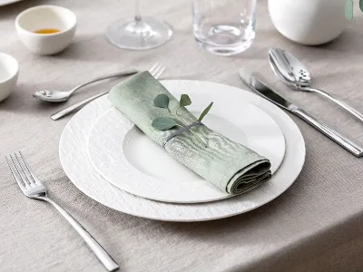 A table set with two white Manufacture plates, a pastel-green napkin, Piedmont cutlery and eucalyptus.