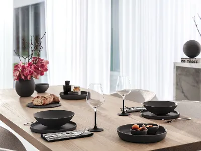 A wooden dining table set with a Villeroy & Boch black La Boule, Manufacture glasses and Piemont cutlery.