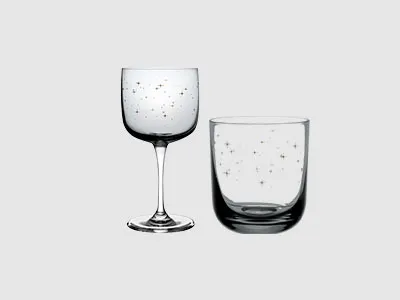 Ein Weinglas und ein Becher, beide durchsichtig mit kleinen Punktmustern, stehen vor einem schlichten hellen Hintergrund.