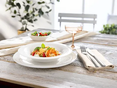 A plate of pasta with vegetables and herbs, a salad and a drink on a wooden table set for one person.