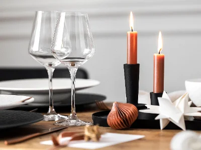 Verres à vin La Divina de Villeroy & Boch, un bougeoir noir avec deux bougies allumées, le tout élégamment entouré d'éléments décoratifs.	