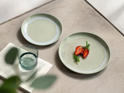 A close-up table view with soft green Perlemor Alga plates by Villeroy & Boch, styled with a halved fig for a natural accent. The setting is completed by a Like Sage water glass, creating a calm, refined atmosphere where organic shapes and earthy tones come together in perfect harmony.
