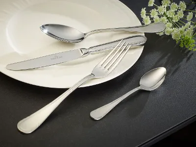 A white plate with cutlery items from the Kreuzband Septfontaines collection on a black surface.