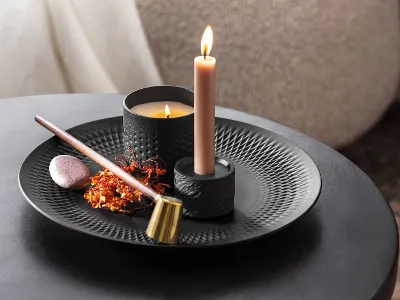 Une bougie allumée avec de l’encens et des fleurs séchées sur une assiette noire décorative Manufacture.