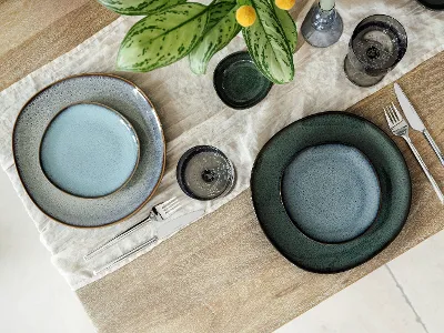 Vue de dessus d’une table moderne avec assiettes à dîner et à pain des collections Lave Vert, Lave Beige et Lave Glacé de Villeroy & Boch. La composition met en valeur les émaux réactifs uniques et les textures naturelles de chaque assiette sur une table neutre, sans nourriture, soulignant l’élégance artisanale du grès.