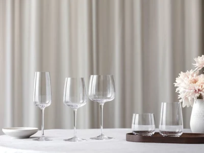 Elegant table setting with four crystal glasses and a white vase of pink flowers on a white tablecloth against a soft, neutral background.
