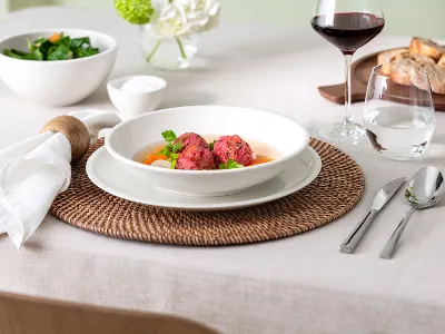 Une table dressée avec un bol Artesano contenant de la soupe, du pain, de la salade, un verre de vin et des couverts sur un set de table tissé.