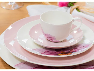 Une tasse, une soucoupe et des assiettes avec un motif floral rose et blanc empilés sur une table en bois