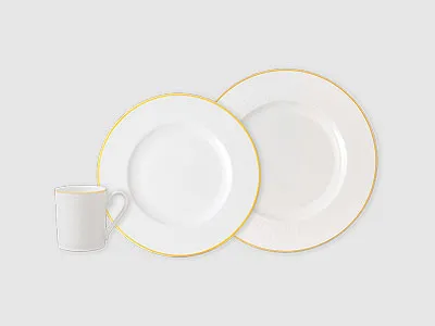 Weiße Tasse und zwei weiße Teller mit Goldrand auf neutralem Hintergrund.
