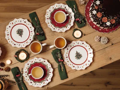 Festive holiday table setting with Toy’s Delight plates, cups of tea, a chocolate cake, and candles on a wooden table.