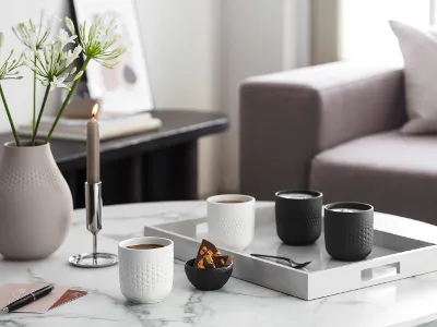 Elegant coffee table in a living room with Manufacture coffee mugs, candles, vases and a tray with cups and snacks.