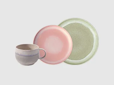 Vor einem hellgrauen Hintergrund sind eine graue Tasse, ein rosa Teller und ein grüner Teller angeordnet.