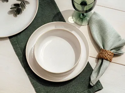 Crafted plate on a green placemat, together with a glass of water and a decorative napkin with a wooden napkin ring.