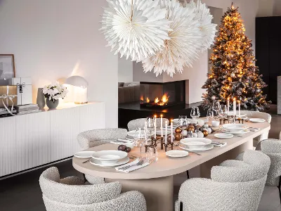 A modern dining room set for a meal with white Afina plates and candles. There are also two large paper stars as decorations, a decorated Christmas tree and a built-in fireplace.