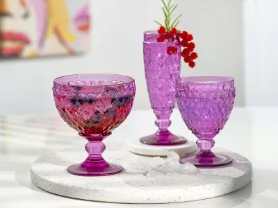 Three different pink Boston glasses with drinks and garnished with berries on a stone tray