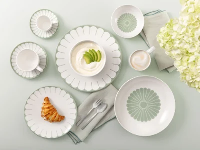Table setting with Villeroy & Boch Fleur Vert plates, croissant, yogurt, coffee, and white flowers on a light green background.