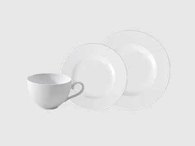 Eine weiße Tasse und zwei weiße Teller werden vor einem schlichten hellen Hintergrund präsentiert.