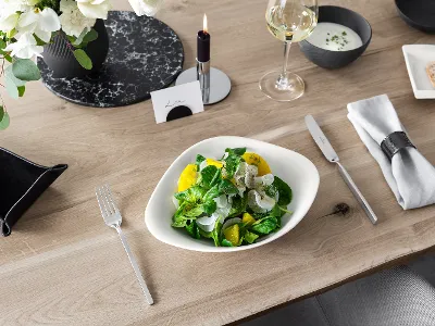 A Villeroy & Boch Vapiano bowl with salad on a wooden table, beside a NewWave knife and fork.