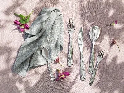 Posate Rose Garden e tovagliolo grigio su una superficie strutturata rosa con fiori e rami sparsi.