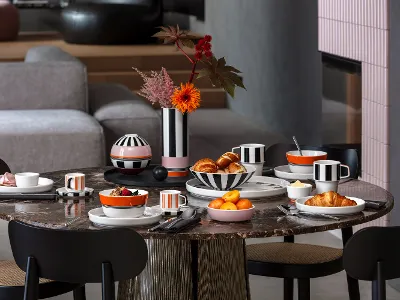 Un tavolo rotondo per la colazione con croissant, frutta, caffè e stoviglie a righe bianche e nere della collezione Memphis di Villeroy & Boch.
