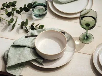A white Crafted Bol on a Crafted plate covered with mint green napkins and eucalyptus.